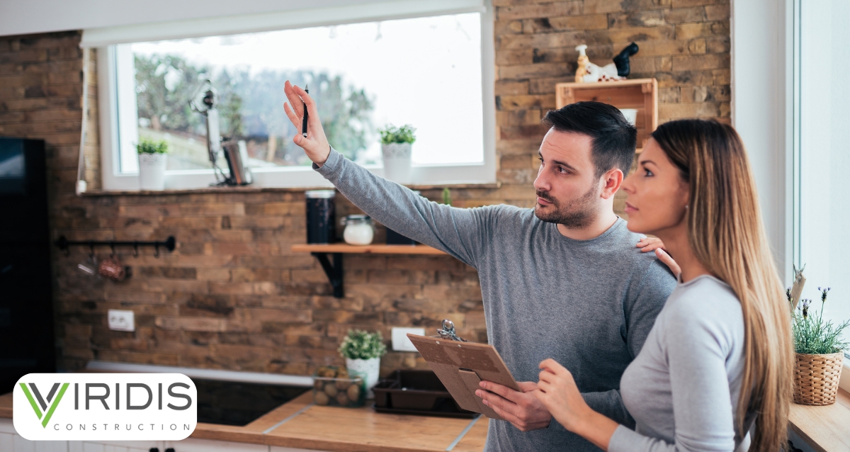A contractor discussing home renovation plans with a homeowner, pointing out areas for improvement inside a modern kitchen with wooden accents. Highlights winter preparation and Viridis Construction’s expertise in personalized home services.
